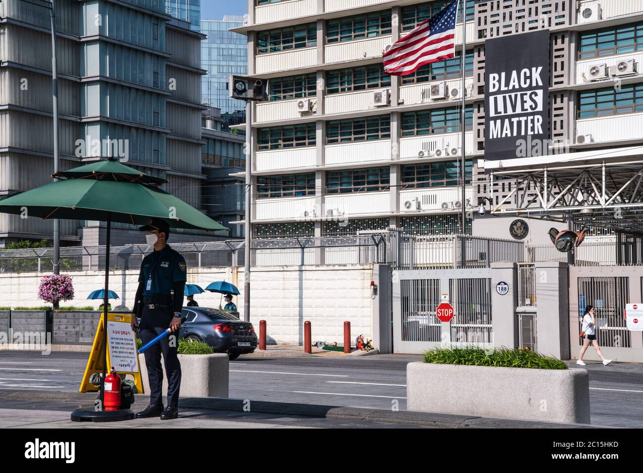 Un ufficiale di polizia che indossa un facemask è visto in piedi in guardia presso l'edificio delle ambasciate degli Stati Uniti a Seoul, dove un banner Black Lives Matter e una bandiera degli Stati Uniti sono appesi. UN banner Black Lives Matter (BLM) è appeso sulla facciata dell'edificio delle ambasciate degli Stati Uniti nel centro di Seoul in solidarietà Con i manifestanti BLM che chiedono un cambiamento positivo. Foto Stock