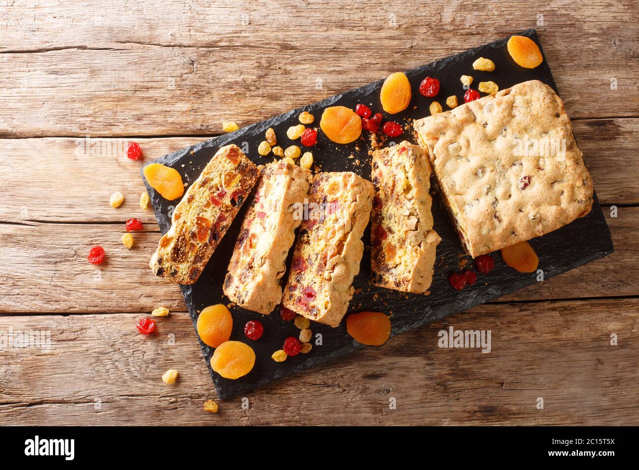 Torta di frutta senza zucchero a fette con albicocche secche, bacche di uva passa fichi ciliegie chiodate su un pannello di ardesia sul tavolo. Vista orizzontale dall'alto Foto Stock