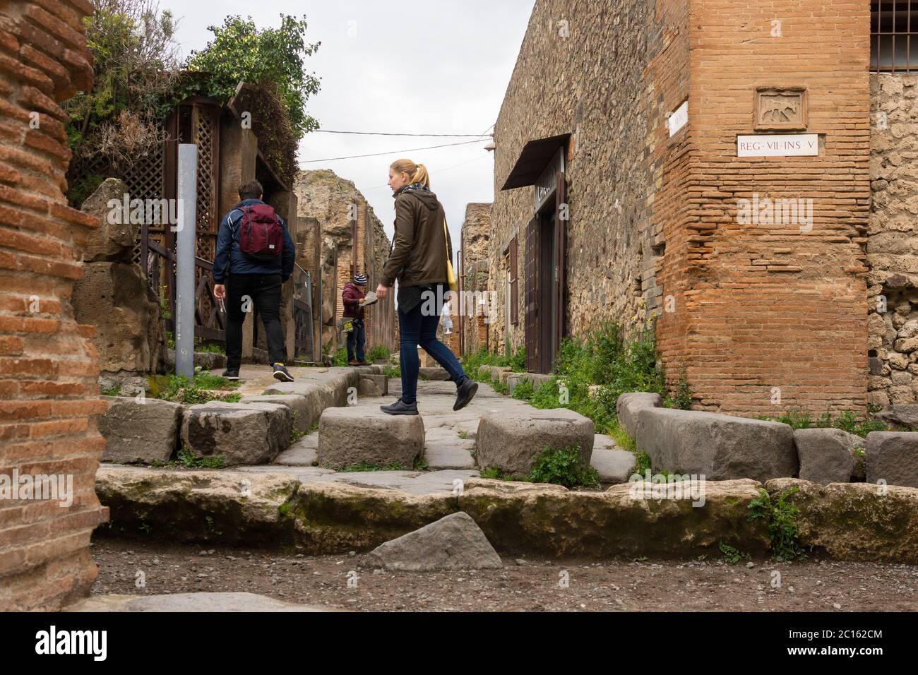 Un visitatore dell'antica città di Pompei cammina sulle pietre a gradini utilizzate dai pedoni per attraversare le strade senza scendere in esse. Italia Foto Stock