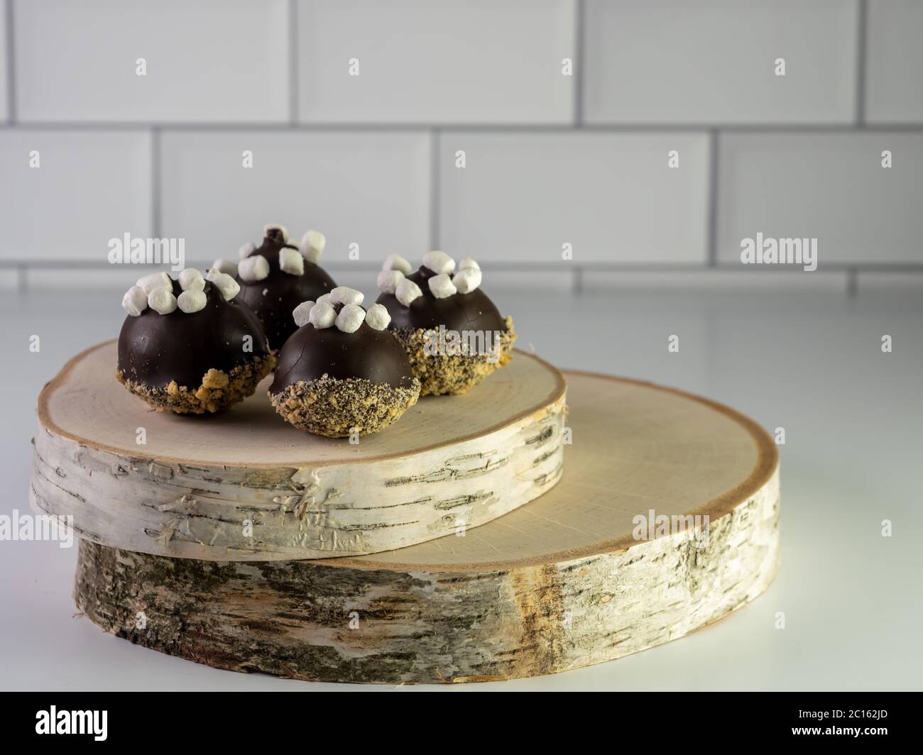 S’MORS palle da torta con un cracker graham e rivestimento al cioccolato e piccoli mini marshmallow in cima seduti su due pezzi di legno reale su un conteggio bianco Foto Stock