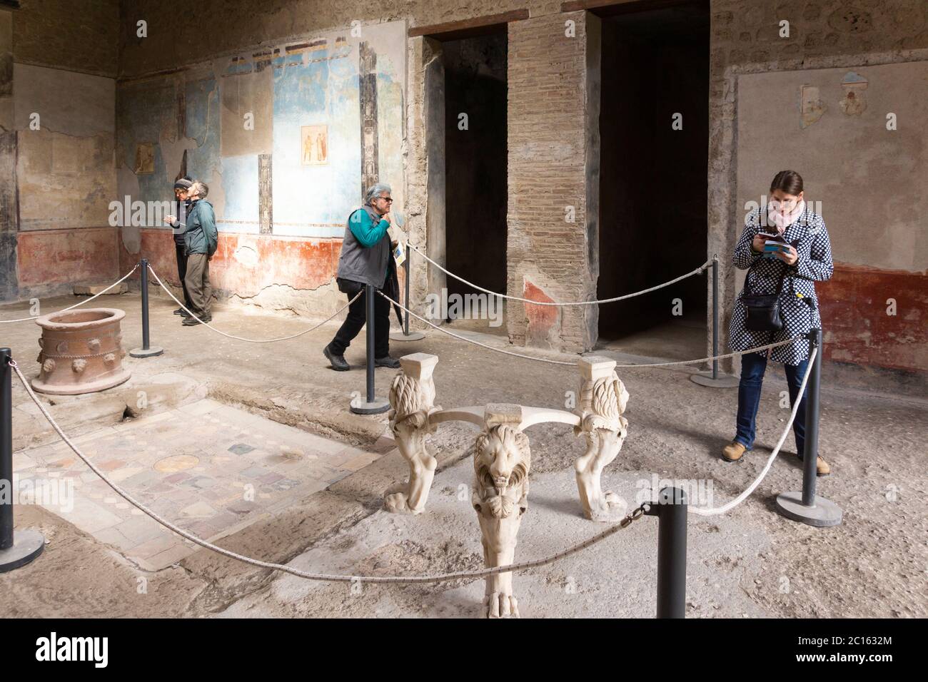 I turisti esplorano la casa di Casca Longus con pareti affrescate dipinte e un tavolo con tre supporti in marmo a forma di zampe di leone. Pompei, Italia Foto Stock