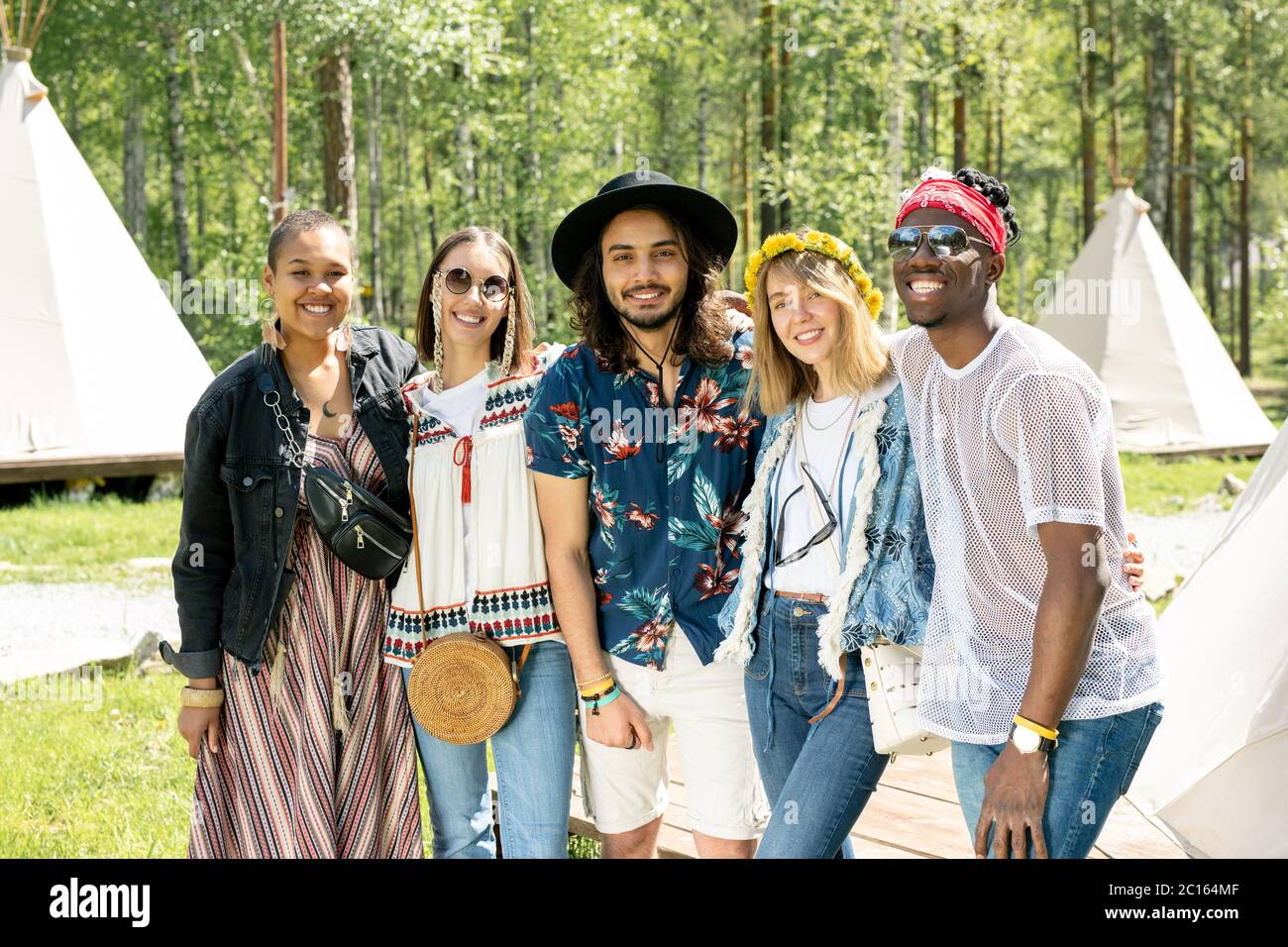 Ritratto di allegri giovani amici multietnici in abiti hippie abbracciarsi l'un l'altro al festival nel campeggio foresta Foto Stock