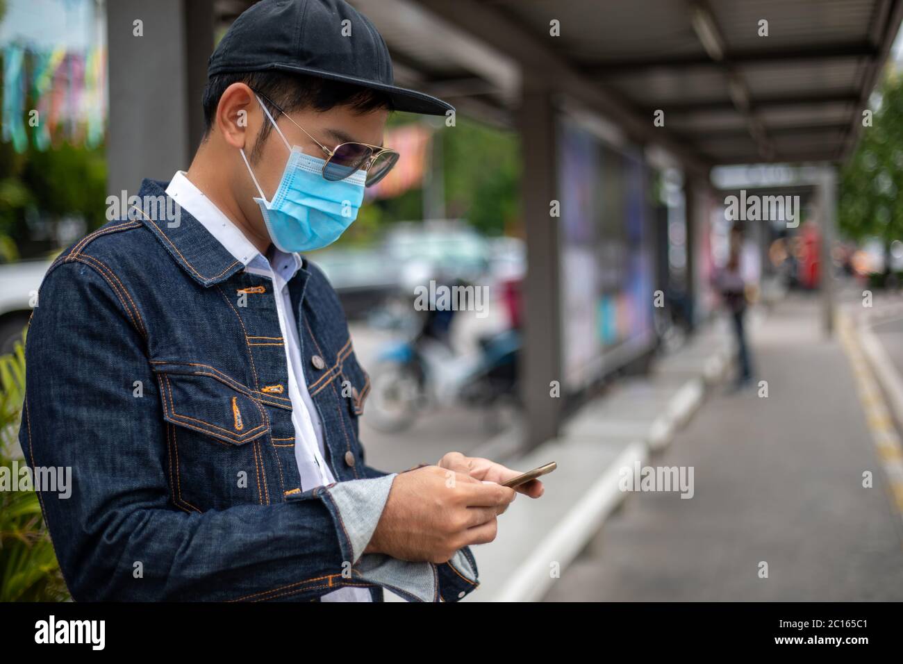 Asian Young man che usa lo smartphone in città e indossa la maschera facciale per la protezione dell'inquinamento atmosferico, delle particelle e per la protezione del virus influenzale, dell'influenza Foto Stock