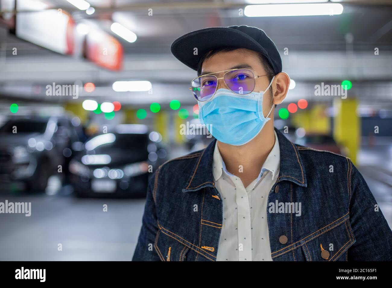 Asian giovane uomo in piedi in città e indossare maschera di protezione sul viso per la protezione dell'inquinamento atmosferico, particolato e per la protezione del virus influenzale, infl Foto Stock