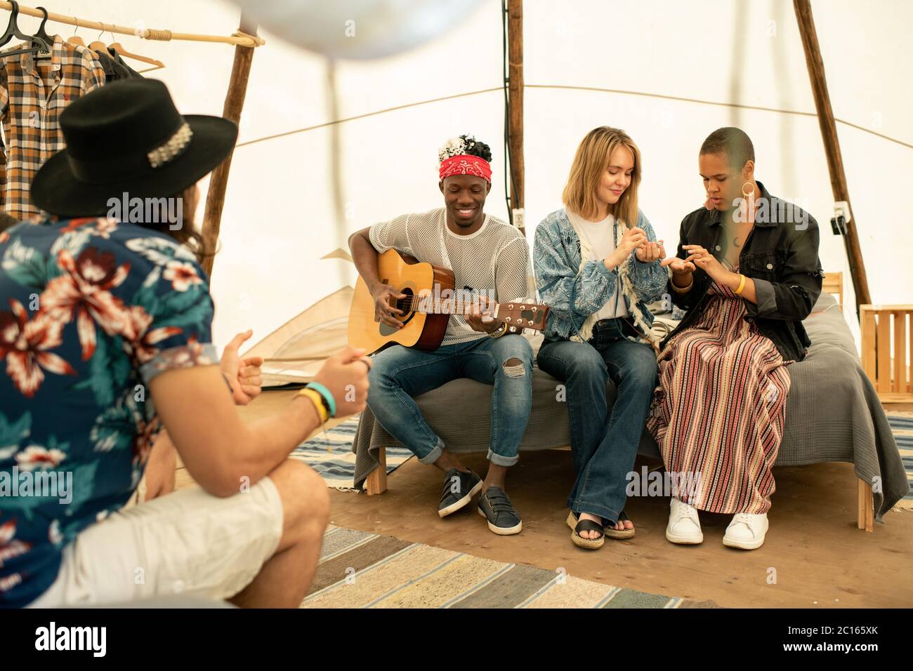 Gruppo di giovani amici multietnici seduti in tenda e ascoltando la musica di chitarra suonata da un ragazzo nero Foto Stock