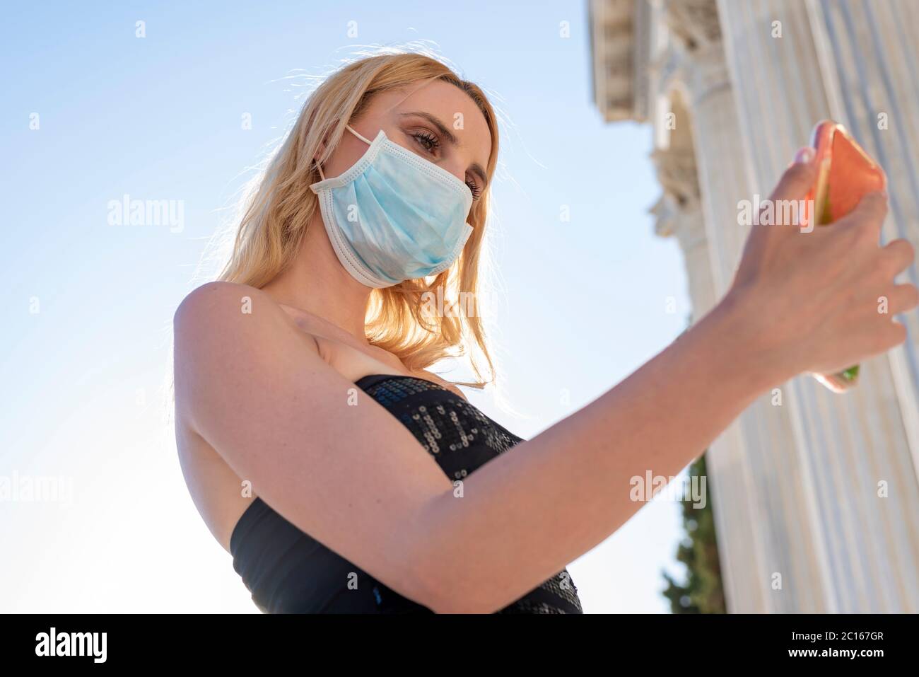 Giovane bionda con maschera facciale utilizzando l'app di tracciamento sullo smartphone mobile - nuovo concetto di stile di vita normale con meleniali che condividono contenuti in questo modo Foto Stock