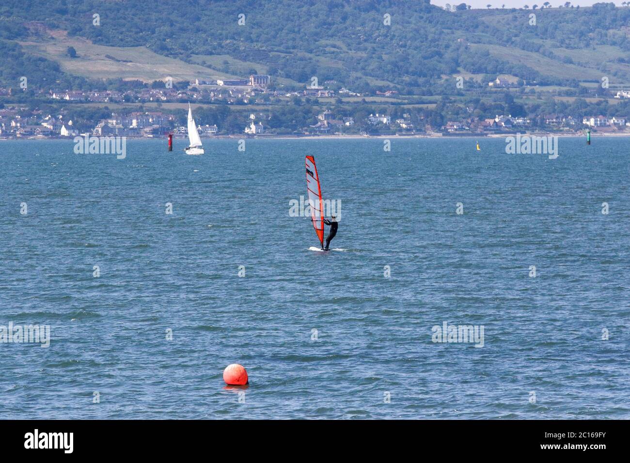 Holywood, County Down, Irlanda del Nord. 14 giugno 2020. Tempo in Gran Bretagna - una calda giornata di sole sulla costa di Belfast Lough nella vicina città di Holywood ha visto la gente fuori provare a godere il bel tempo caldo e soleggiato con le temperature a metà degli anni venti. Windsurf maschile a bordo di una barca a vela rossa a Belfast Lough in un giorno estivo di giugno. Credit: CAZIMB/Alamy Live News. Foto Stock