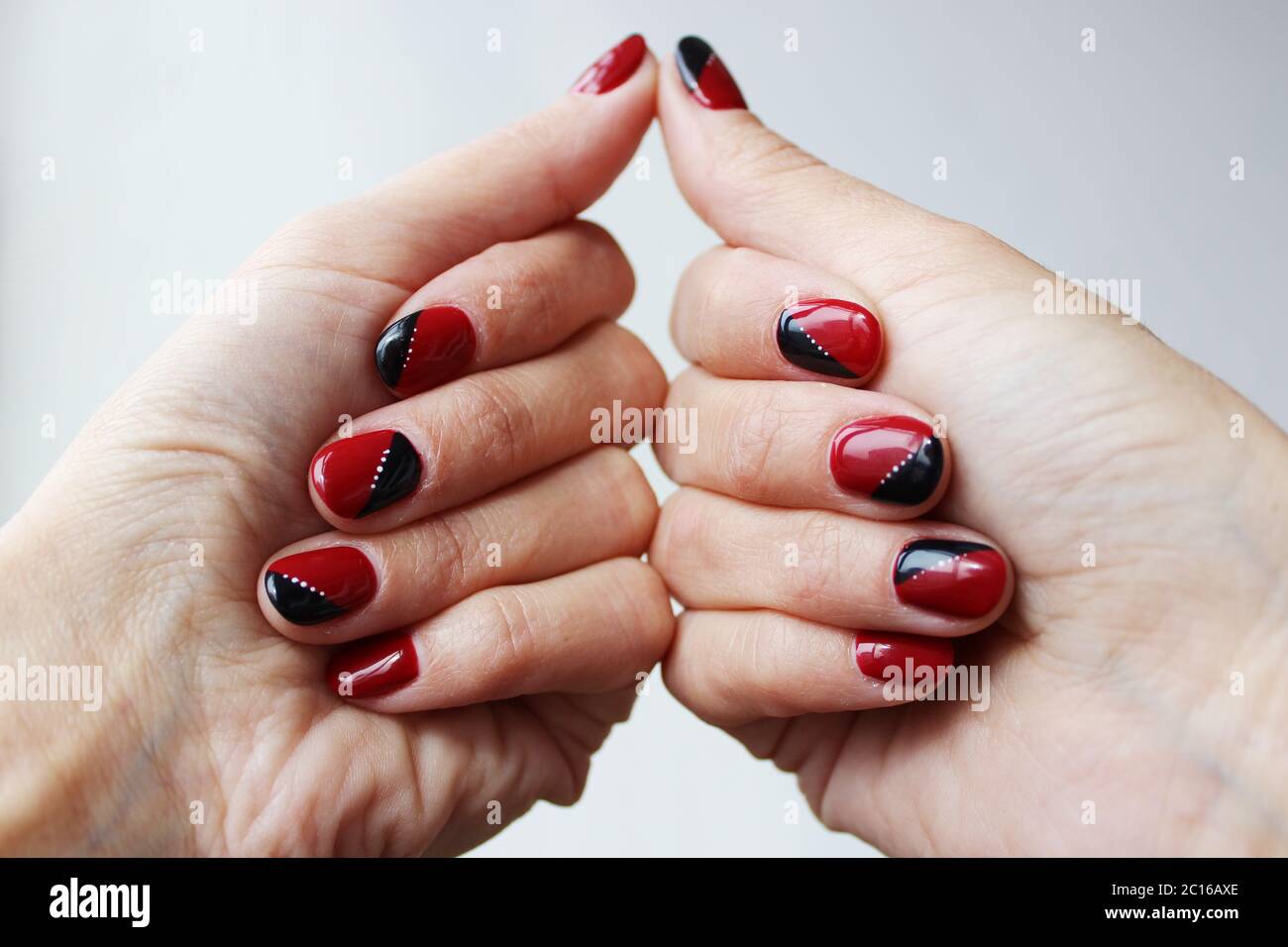 bellezza delicato manicure rosso-nero con vernice gel su fondo bianco Foto Stock