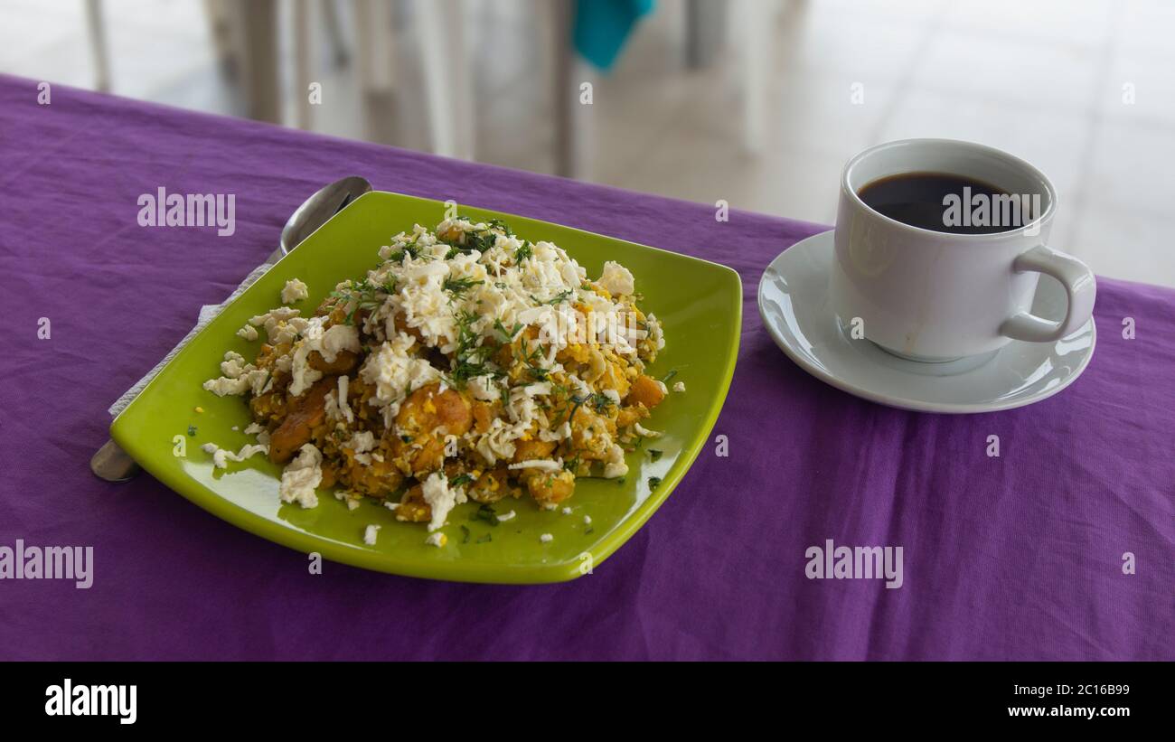 Il TIGRILLEO è un piatto tipico costituito da banana verde macinata con formaggio servito in un piatto verde su un tavolo viola accompagnato da una tazza di caffè wi Foto Stock