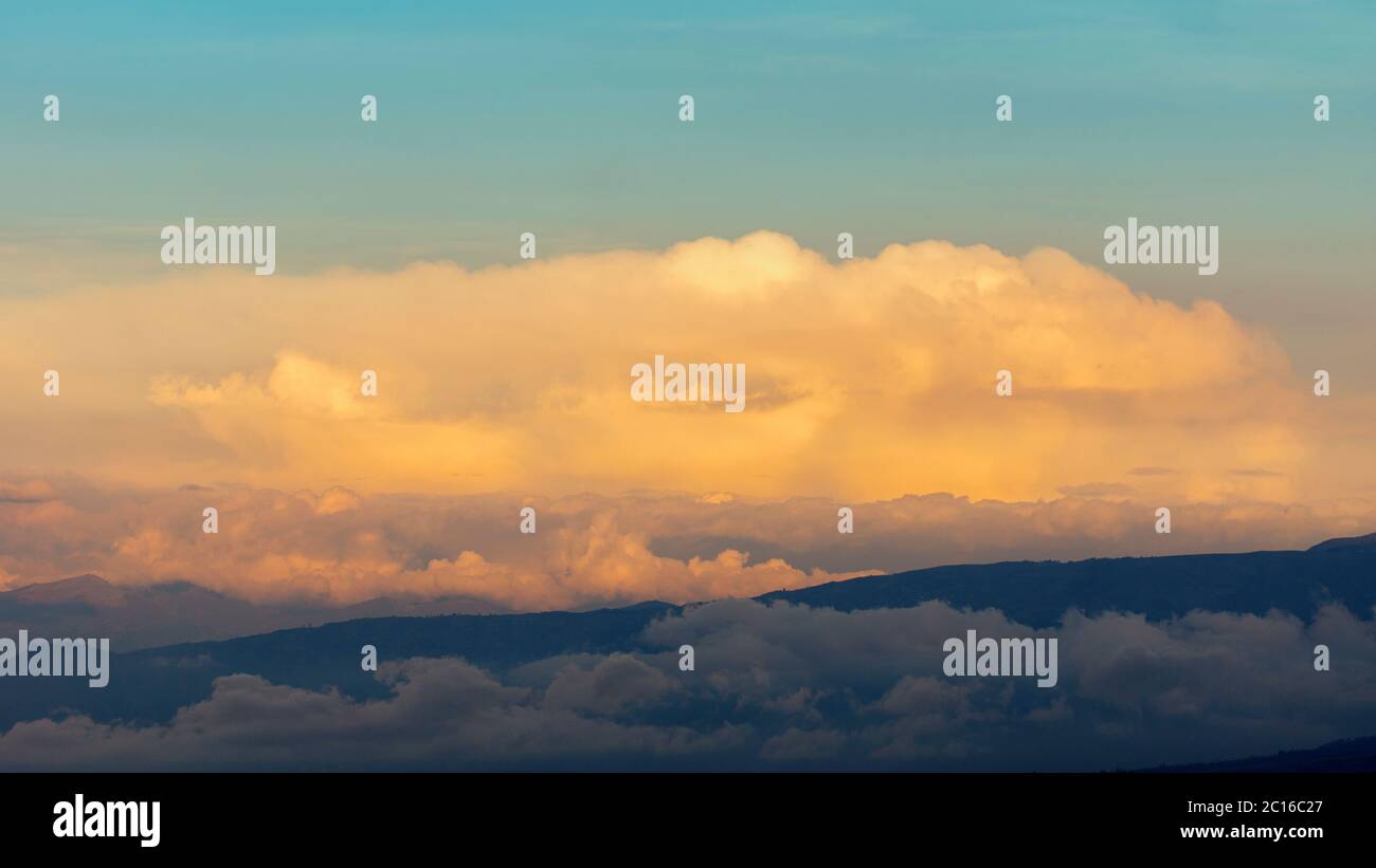Tramonto con silhouette di montagna circondata da nuvole gialle e cielo blu Foto Stock
