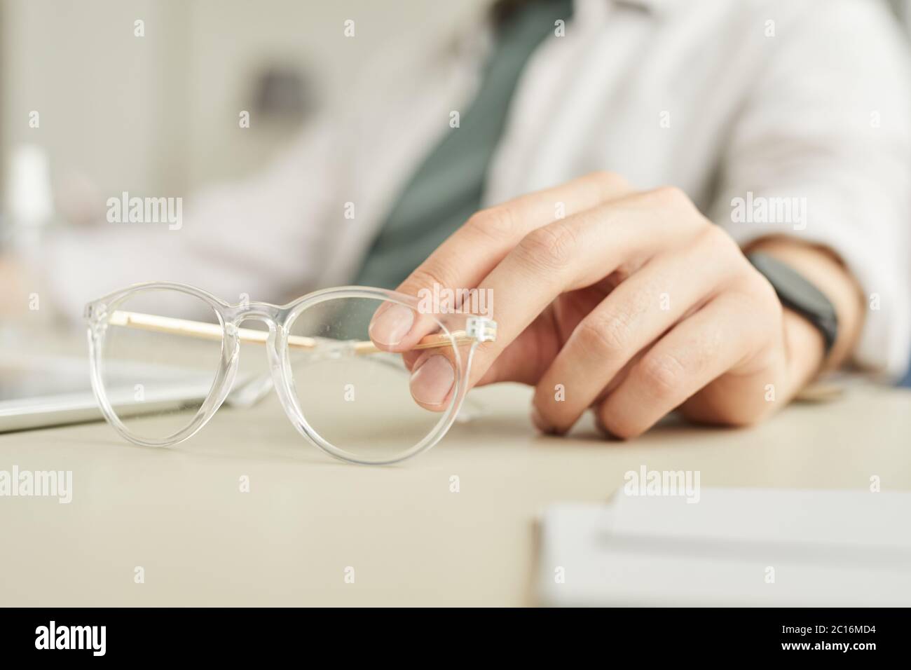 Minimo primo piano di occhiali trasparenti con tenuta a mano mentre si lavora alla scrivania in ufficio, spazio per fotocopie Foto Stock