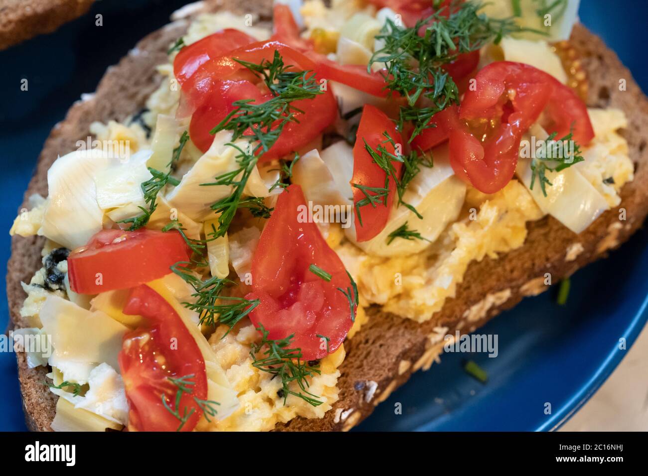 Panino vegetariano / vegano aperto, hummus, pomodoro, carciofo e aneto su pane integrale seminato Foto Stock