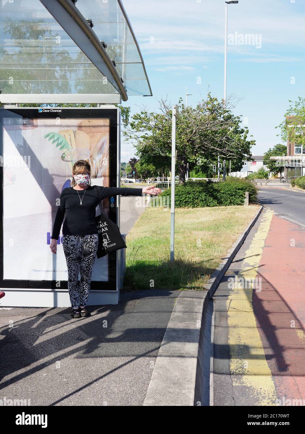 Una donna attende un autobus a una fermata dell'autobus con un viso colorato che copre il 15 giugno 2020 Foto Stock