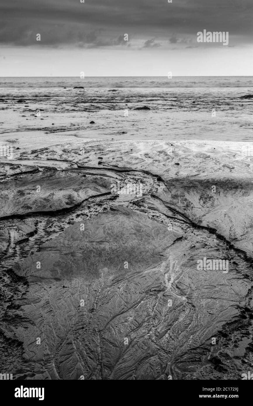 Le acque si ritirano nell'oceano formando delle linee interessanti nella sabbia Foto Stock