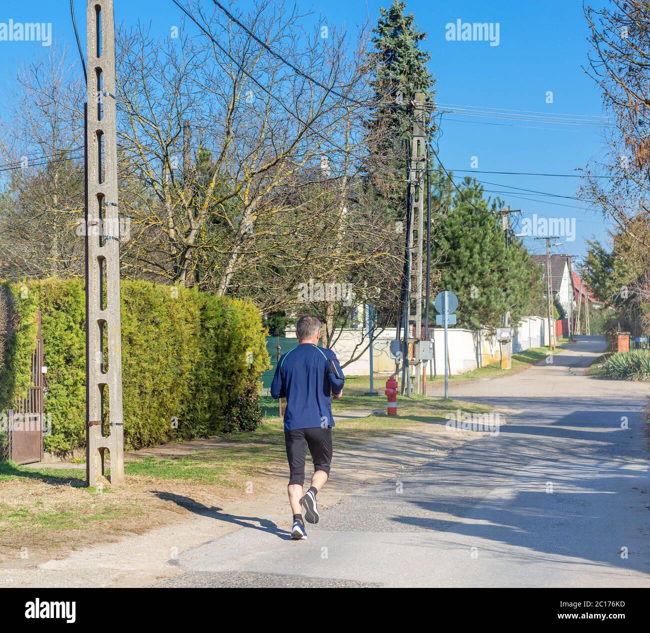 Uomo dai capelli grigi che corre lungo la strada della piccola città. Attività sportive e di stile di vita attivo in concetto di età avanzata Foto Stock