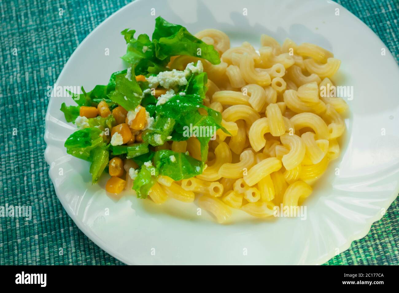 Pasta con guarnitura: Insalata, ketchup, mais, uova strapazzate con cracklings su un tovagliolo blu. Porzione di pasta su un piatto bianco Foto Stock