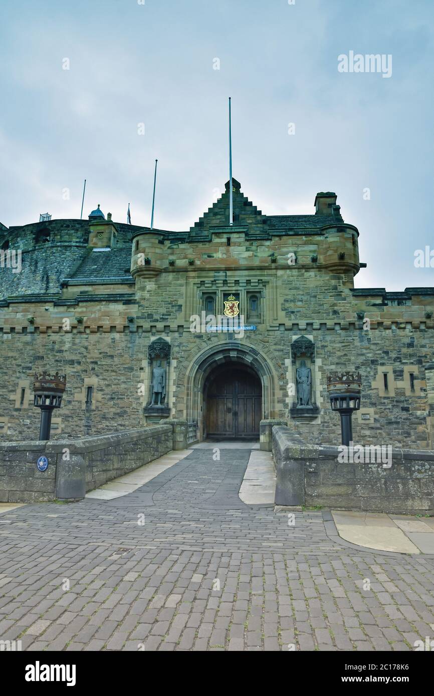 Ingresso al Castello di Edimburgo, Scozia, senza persone, con porta d'ingresso, finestre, torce, percorso acciottolato e torrette. Cielo blu e bianco. Foto Stock
