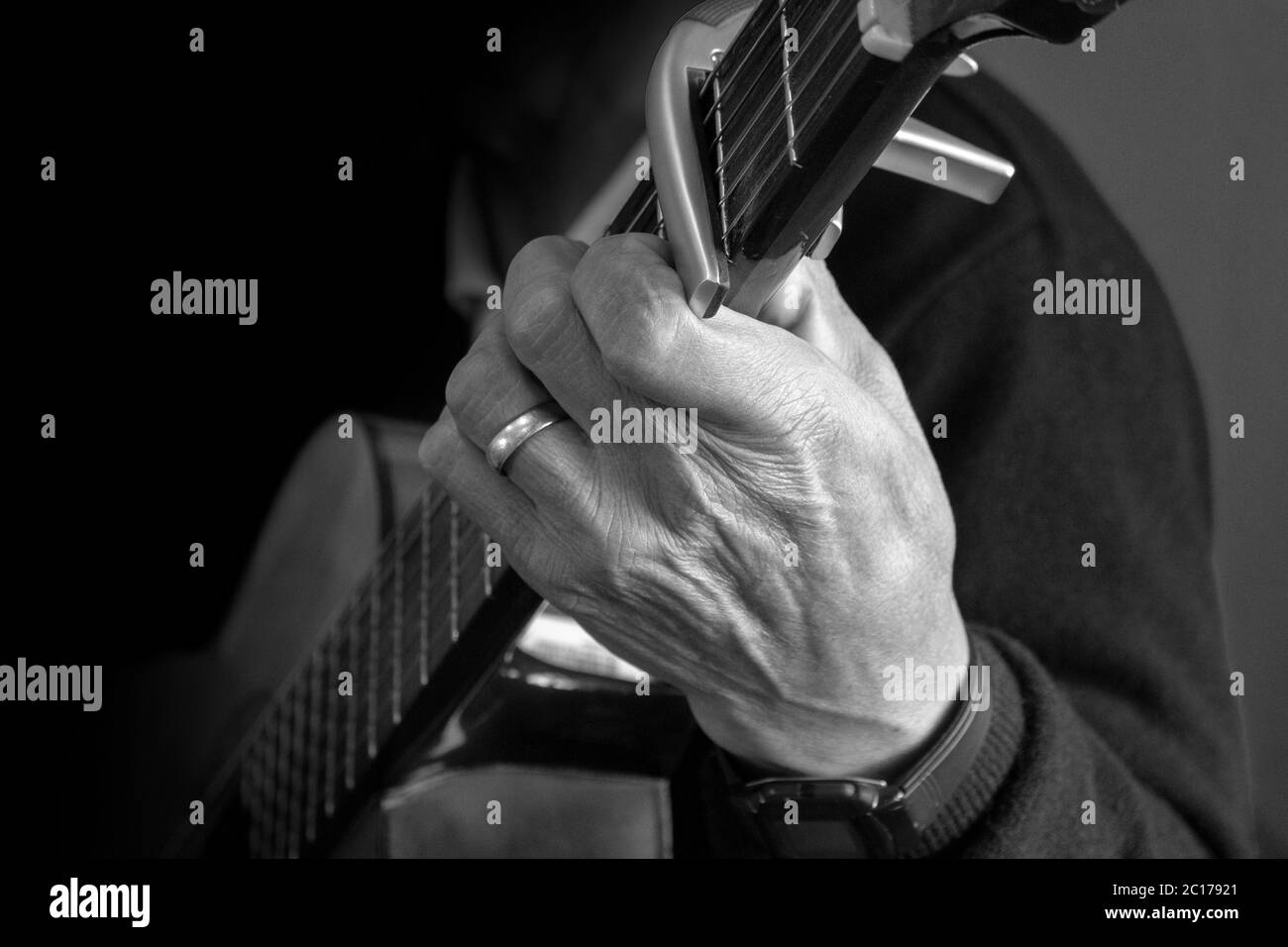 Avvicinati alla mano di un anziano seduto tenendo una chitarra con un anello di nozze sul dito su uno sfondo marrone Foto Stock