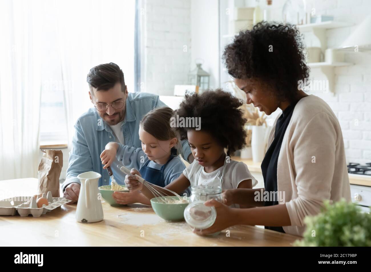 I piccoli aiutanti e i genitori cucinano insieme la torta in cucina Foto Stock
