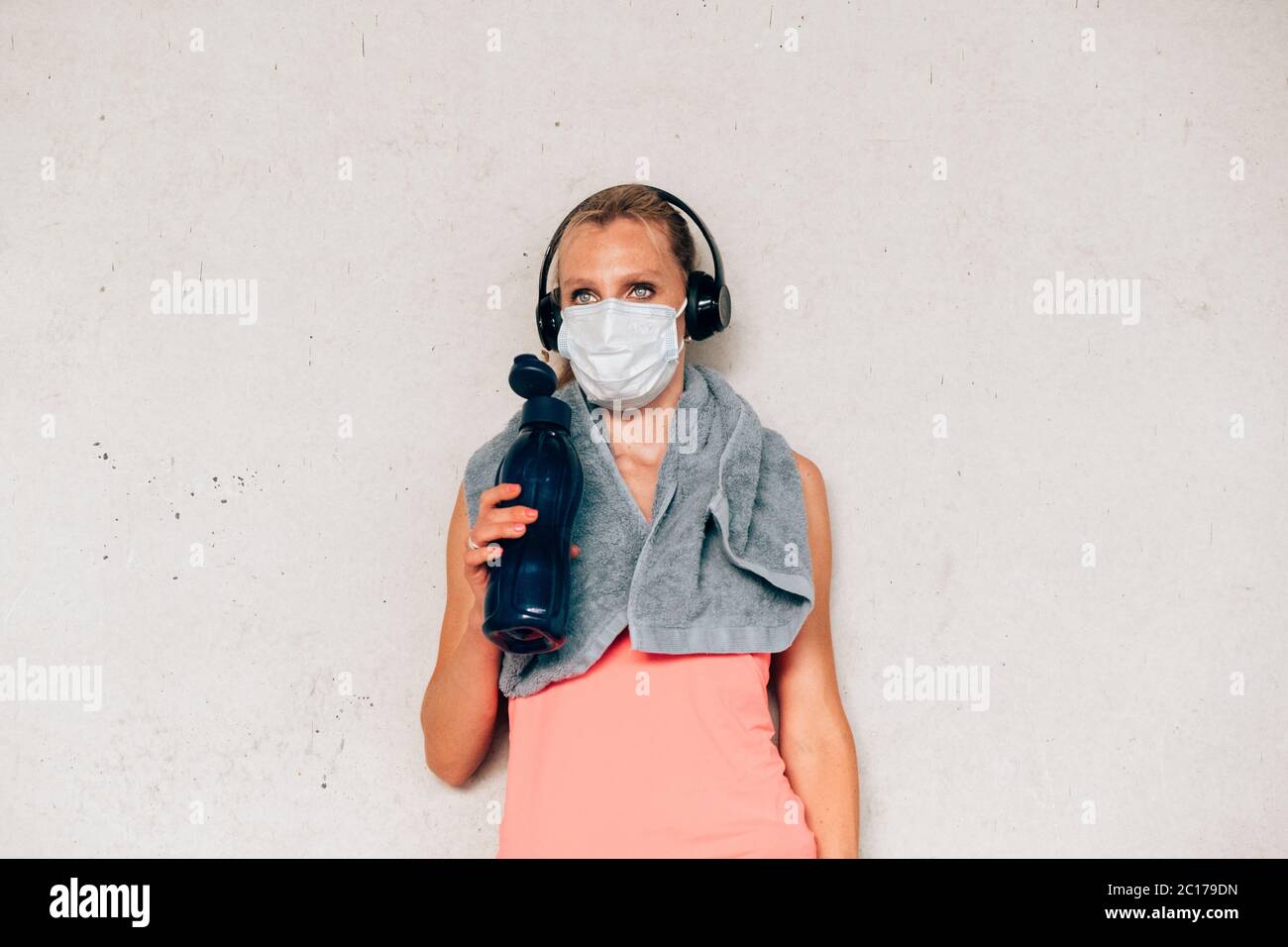 Donna fitness con maschera protettiva in piedi contro un muro in corda. Donna che si riposa dopo aver lavorato su sfondo concreto. Foto Stock