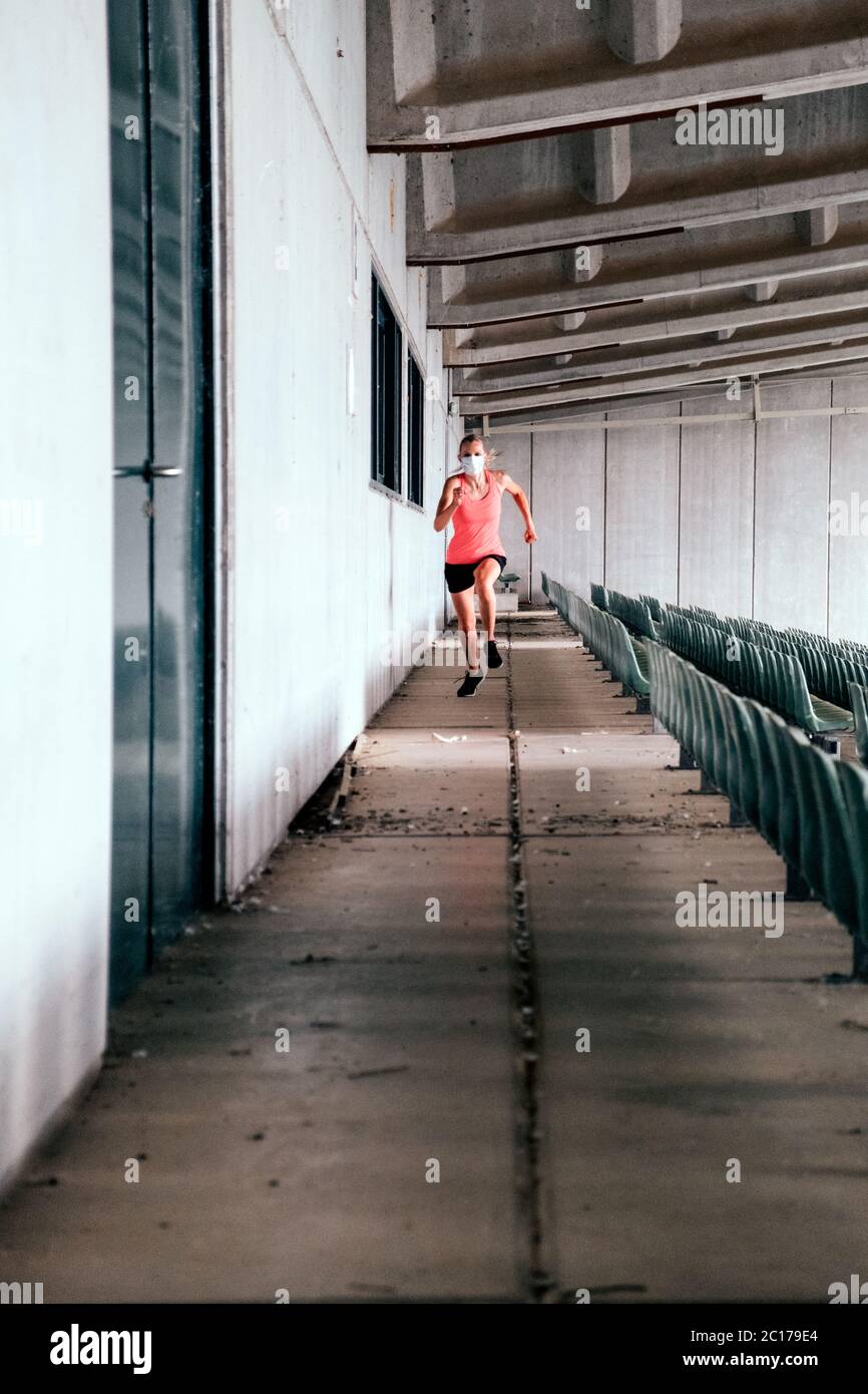 donna in forma sana che fa sport ai gradini dello stadio - corridore femminile allo stadio con una maschera protettiva Foto Stock