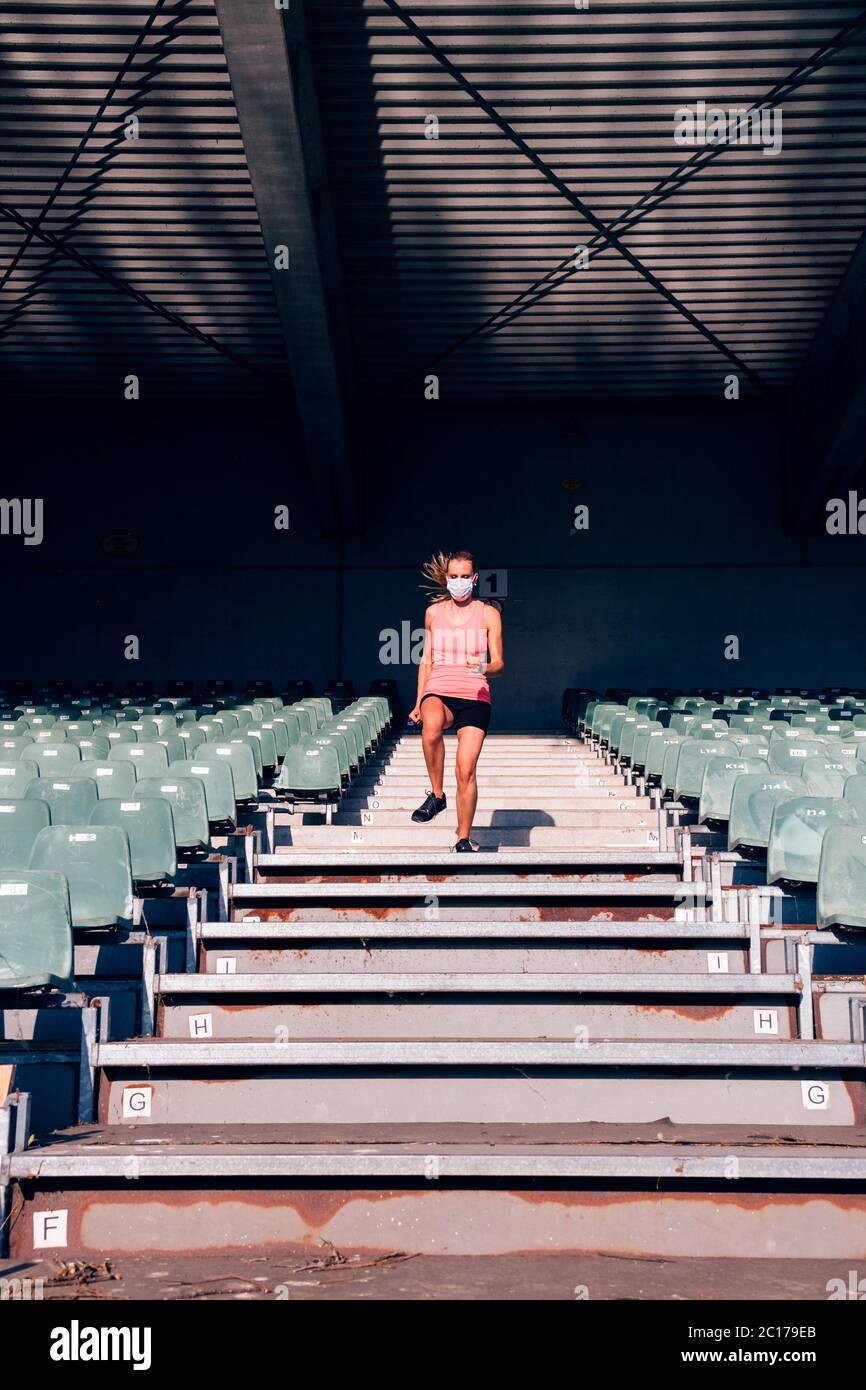 donna in forma sana che fa sport ai gradini dello stadio - corridore femminile allo stadio con una maschera protettiva Foto Stock