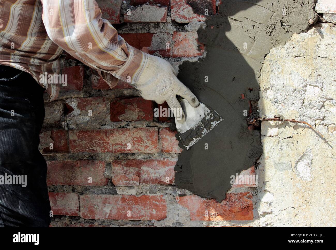 Un muratore professionale muratore con cazzuola di mano applica la Malta di cemento alla parete di mattone davanti al rivestimento durante le res Foto Stock