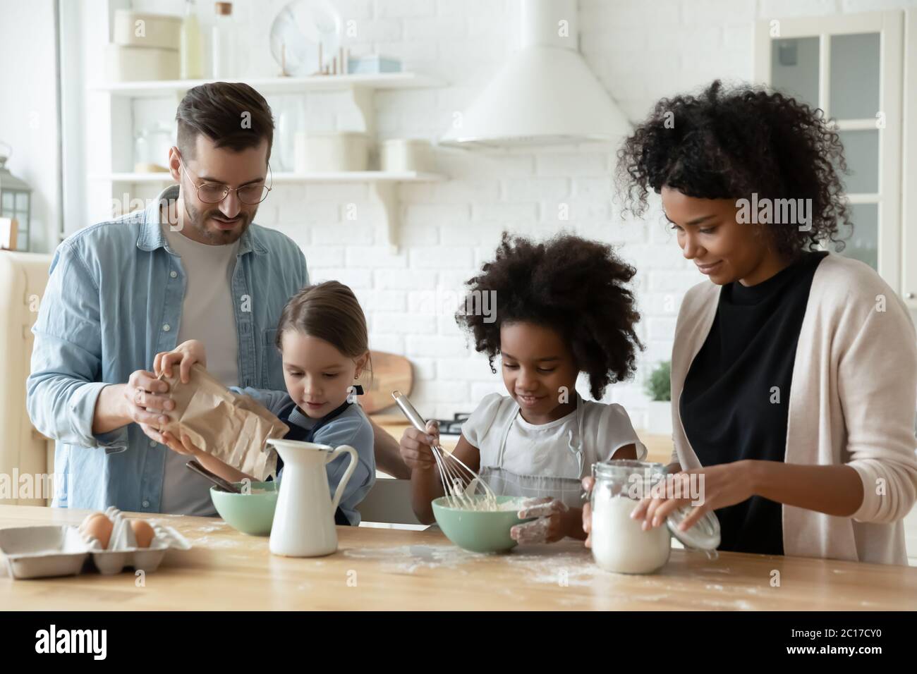 Famiglia multirazziale con i bambini che cucinano dolci riuniti in cucina Foto Stock