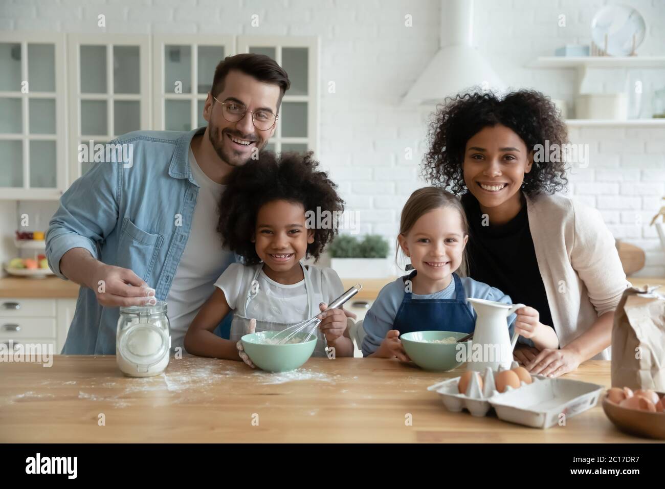 Famiglia multietnica con figlie impegnate nella preparazione di torte in cucina Foto Stock