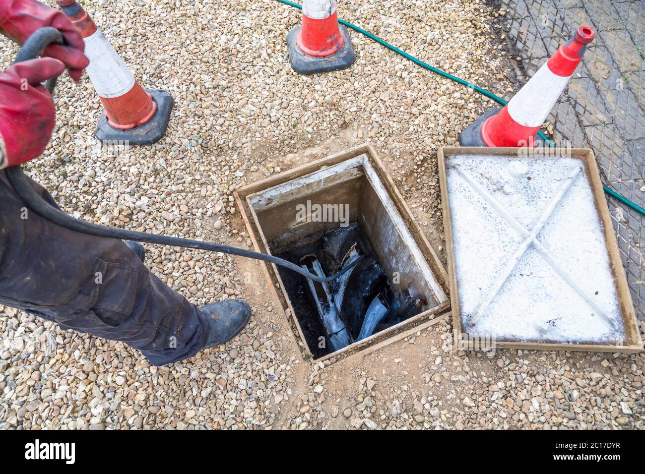 Uomo che sblocca lo scarico delle acque reflue domestiche attraverso la camera di ispezione aperta, società di pulizia scarico, Regno Unito Foto Stock