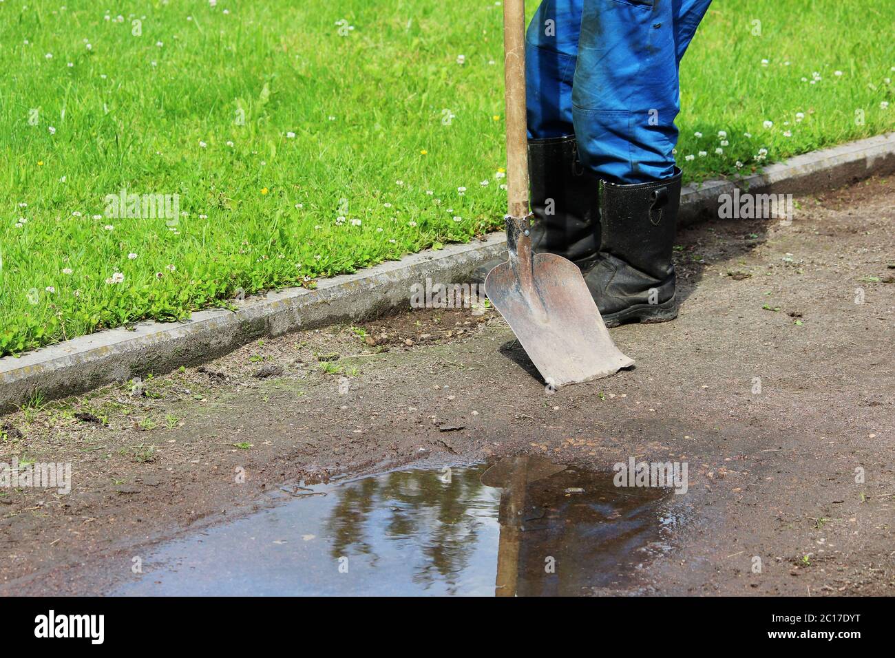 Il lavoratore rimuove l'erba cresce su un sentiero di ghiaia usando una vecchia pala. Foto Stock