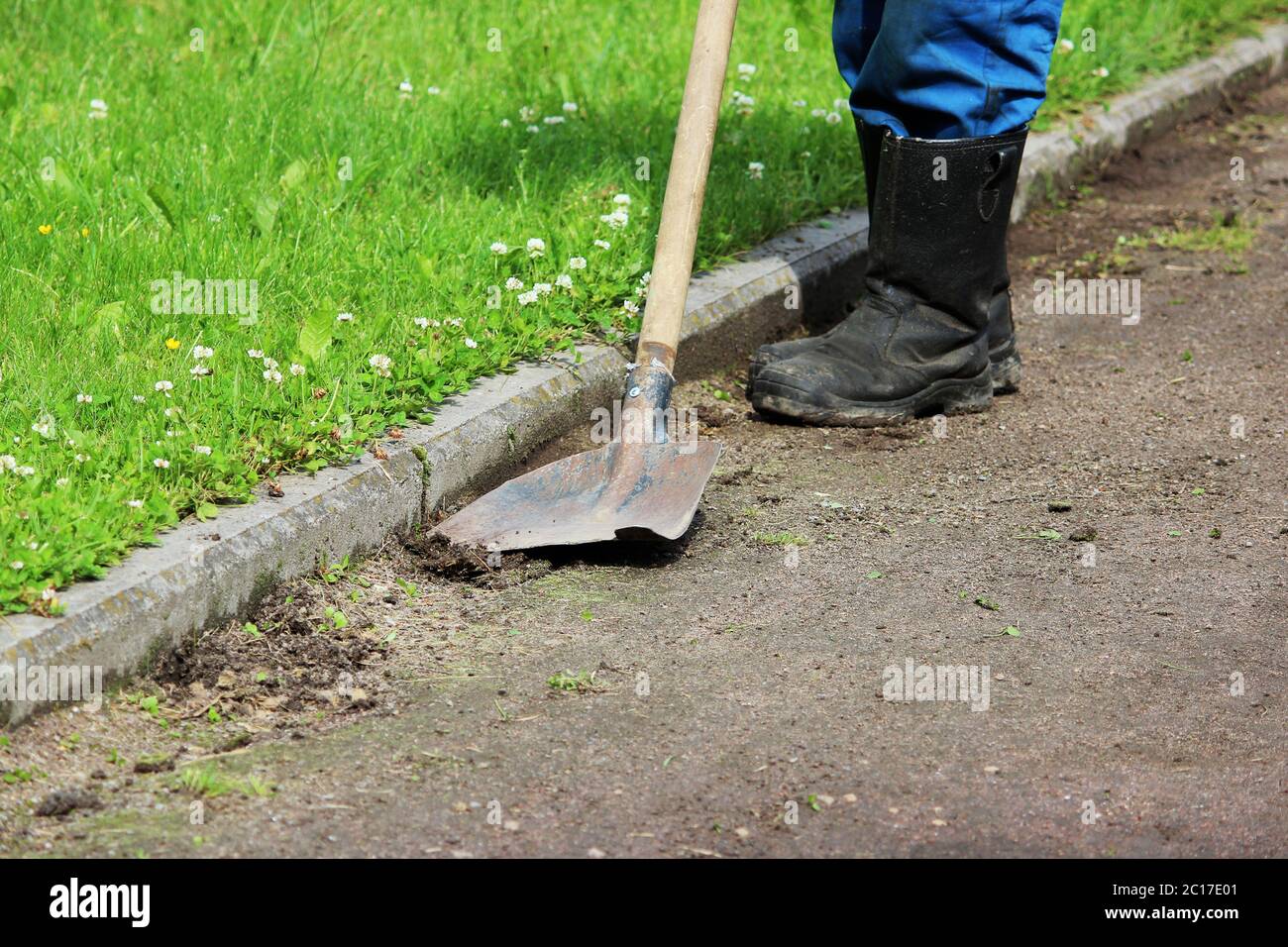 Il lavoratore rimuove l'erba cresce su un sentiero di ghiaia usando una vecchia pala. Foto Stock