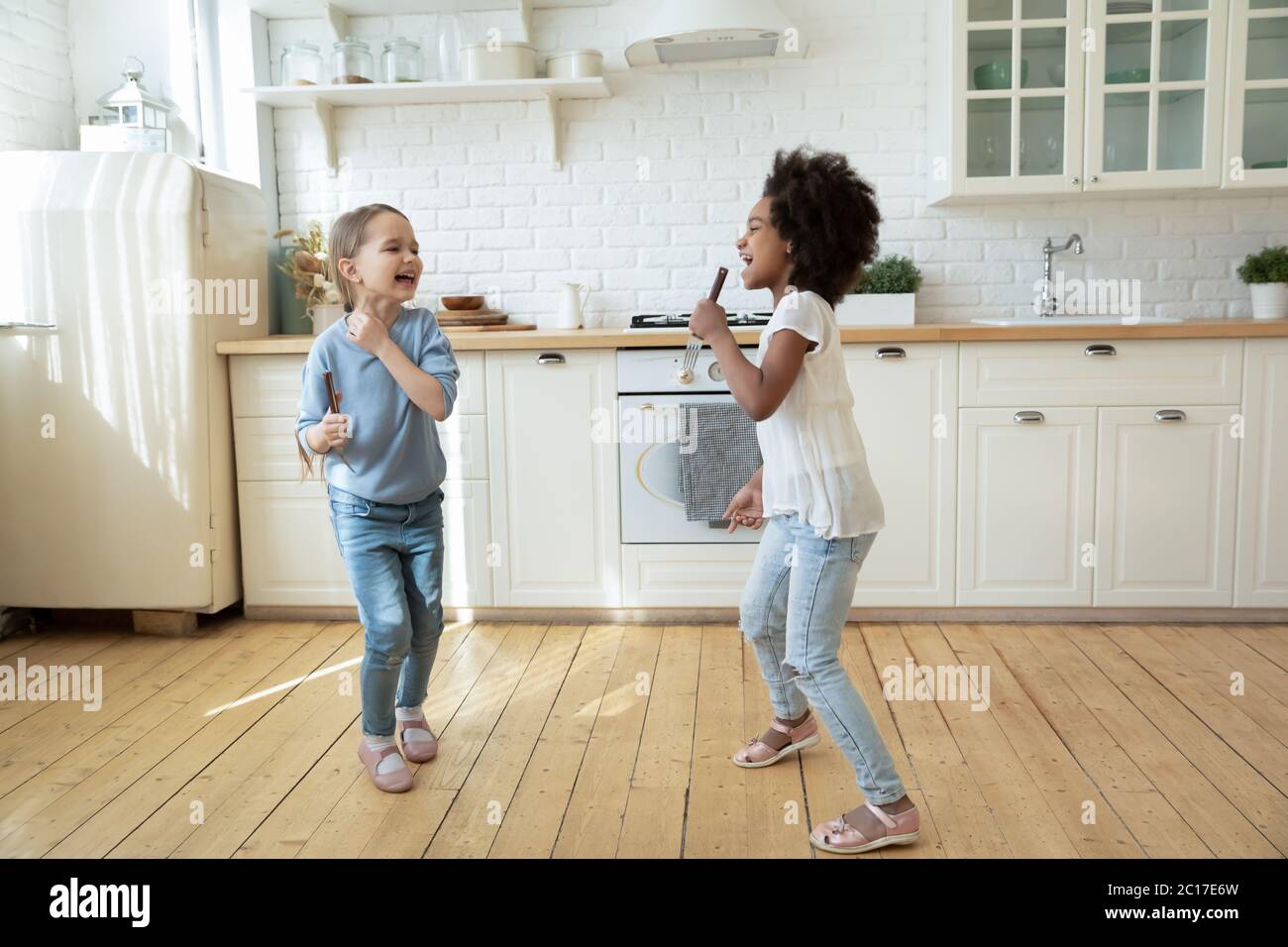 Le ragazze multietniche giocano in cucina cantando canzoni e ballando Foto Stock