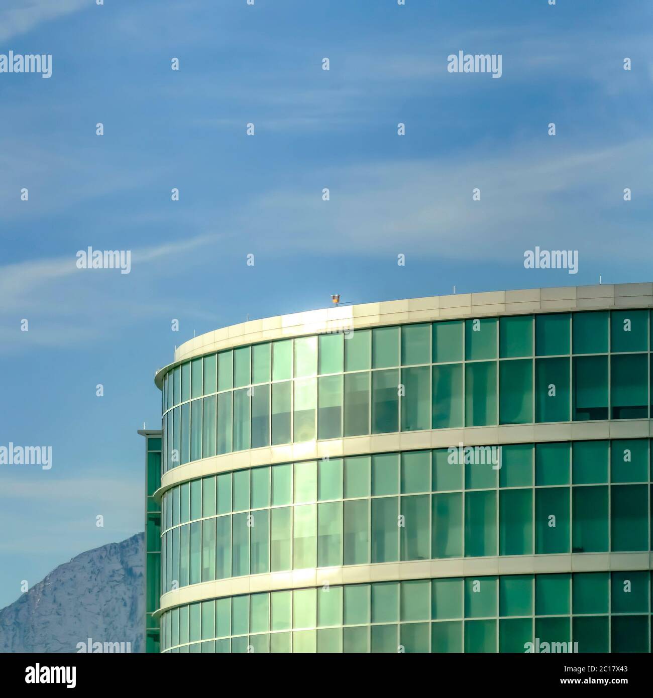 Edificio moderno in vetro commerciale, con montagne innevate e cielo nuvoloso Foto Stock