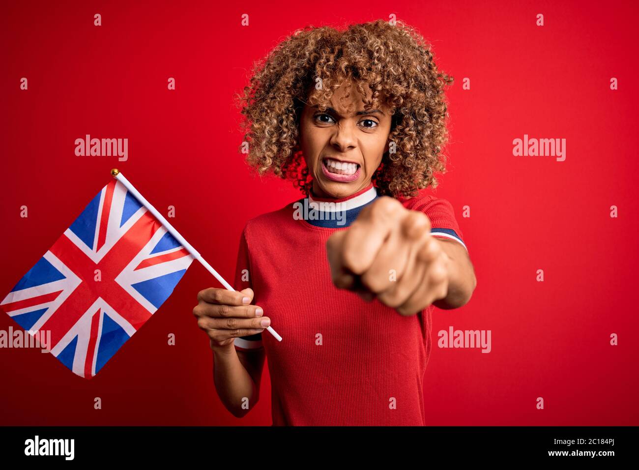 Giovane donna riccia afroamericana che detiene la bandiera britannica per celebrare il referendum sulla brexit infastidita e frustrata gridando con rabbia, pazza e urla con ra Foto Stock