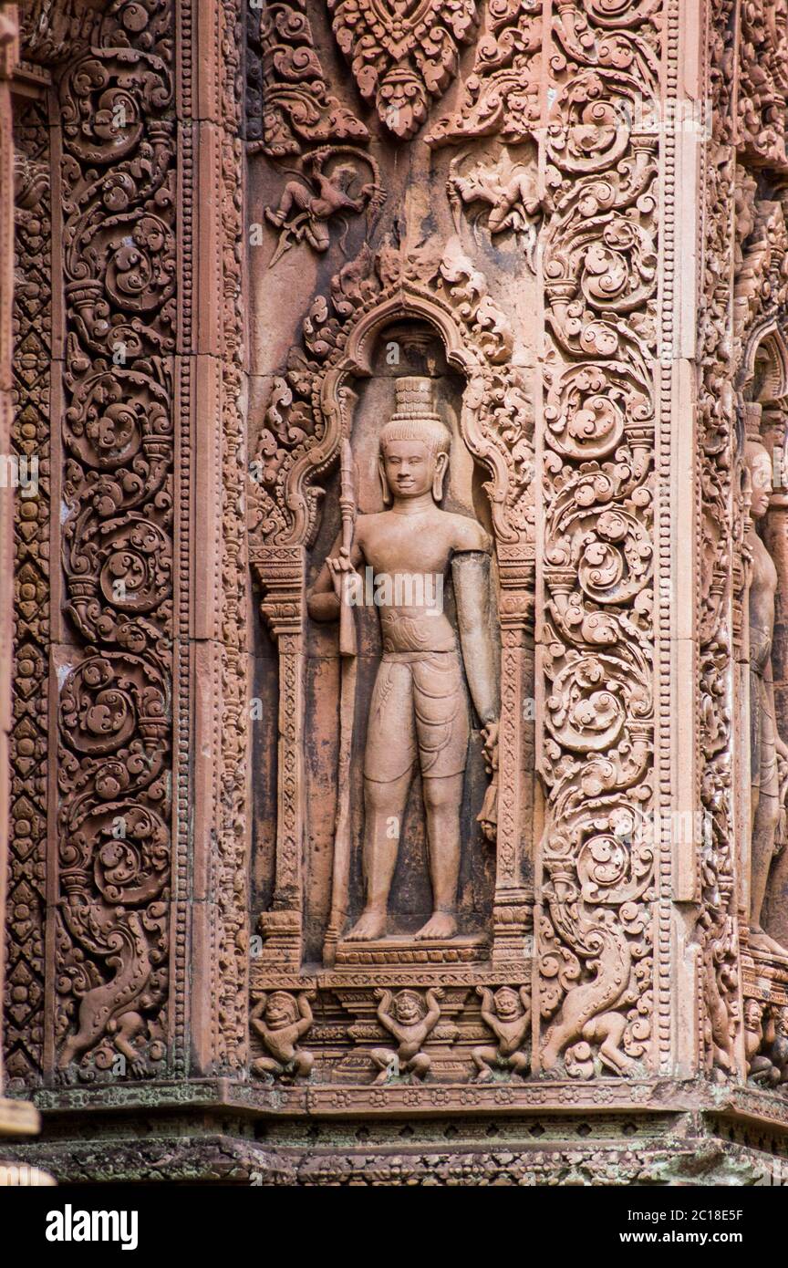 Una scultura custode sulla parete esterna di un prasat, o cappella, al tempio di Banteay Srei, Angkor, Cambogia. Intricato Khmer scultura in arenaria rossa sopra Foto Stock