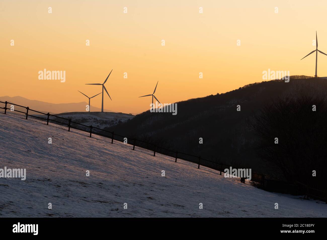 La silhouette dei mulini a vento sulla cima di una montagna da lontano con il cielo arancione del tramonto. Foto Stock