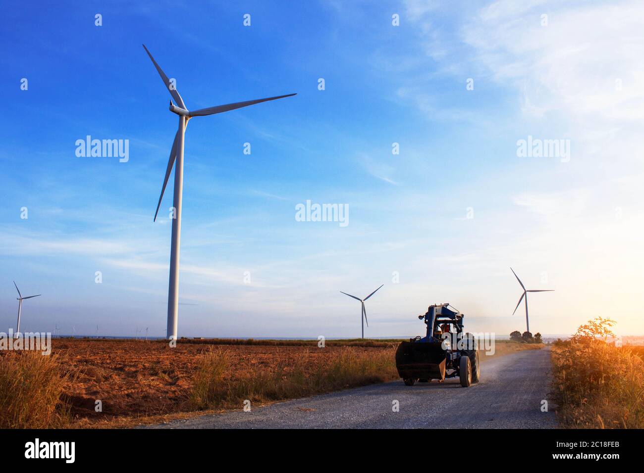 trattori su una strada rurale con un parco eolico. Foto Stock