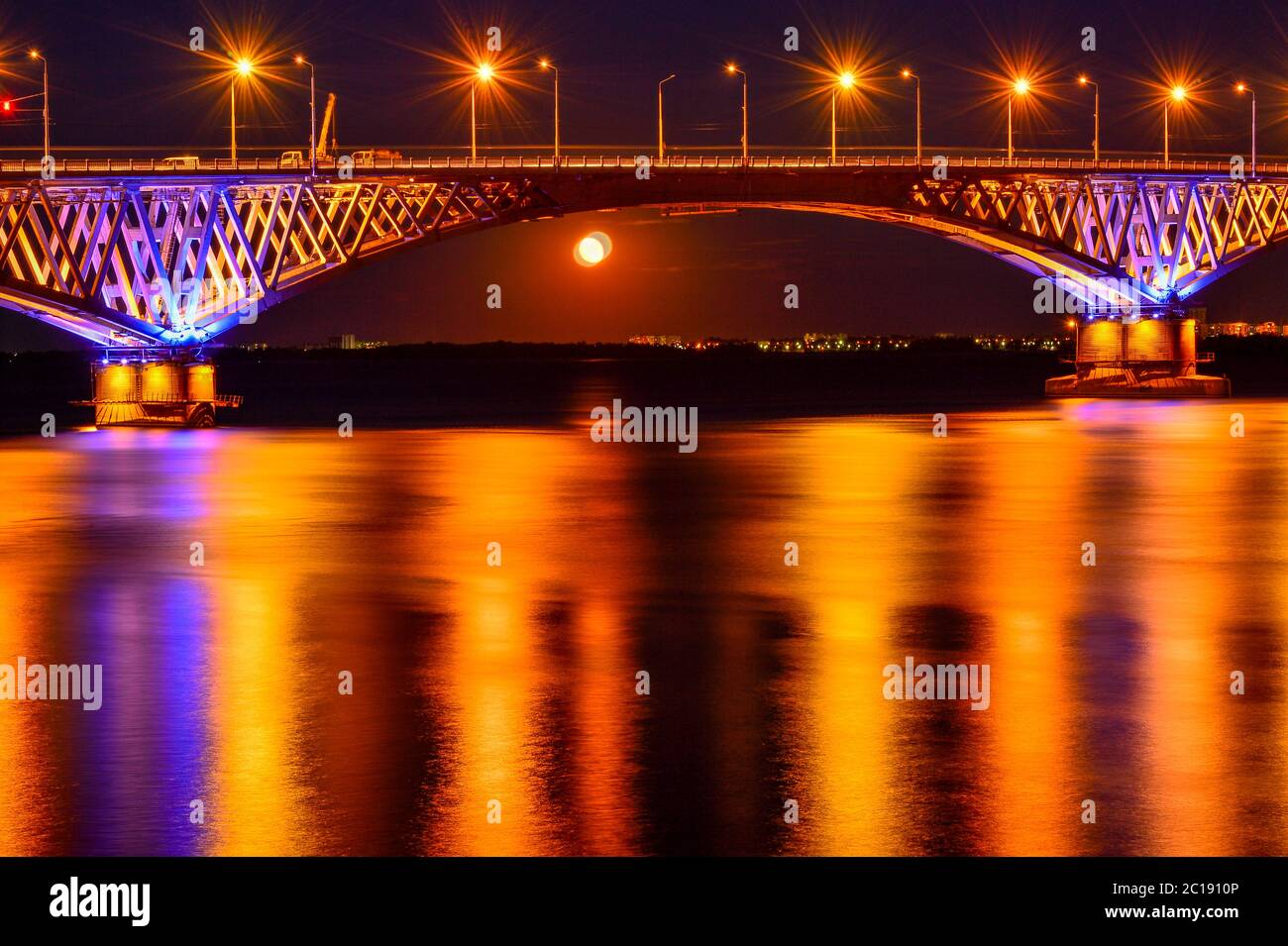 Le luci notturne luminose di un grande ponte sul fiume si riflettono nell'acqua Foto Stock