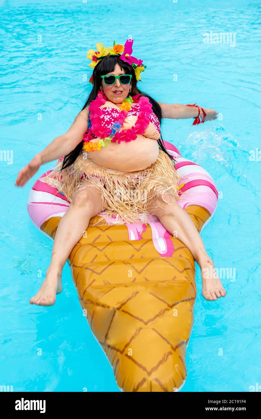 Divertente ritratto di una donna vestita in costume Hawaiiano che galleggia su un gelato gonfiabile a forma di piscina Foto Stock