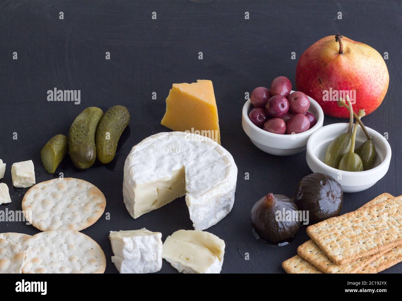 Formaggio, cracker, pera, aneto, olive, fichi e frutti di bosco su fondo nero con spazio Foto Stock