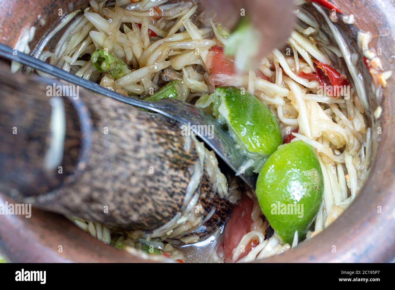 Preparazione della popolare insalata di papaya tailandese, gli ingredienti freschi sono smaschiati con pestello in mortaio, primo piano. Foto Stock