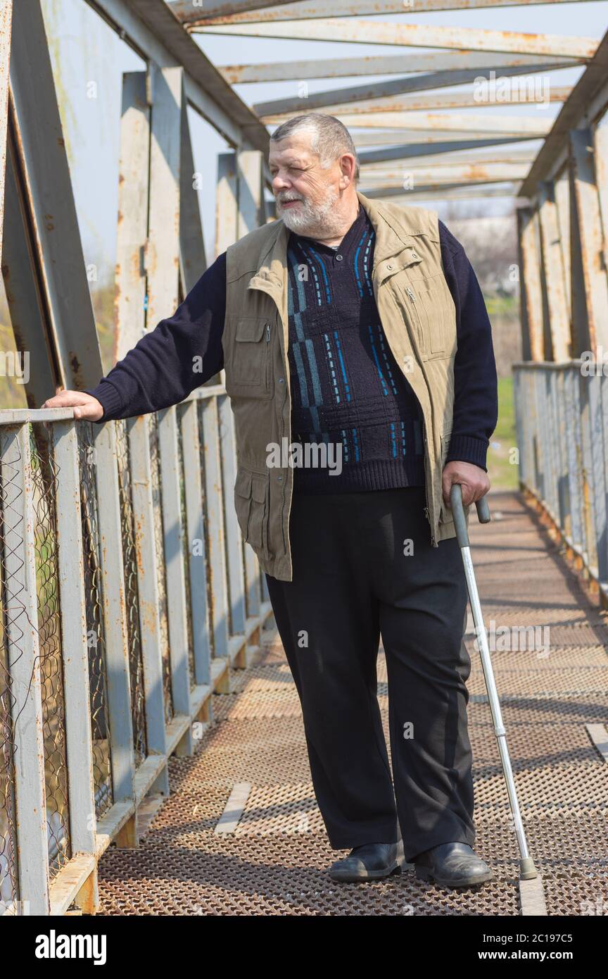 Uomo caucasico anziano con bastone in piedi su un ponte di metallo sul piccolo fiume Sura in Ucraina Foto Stock