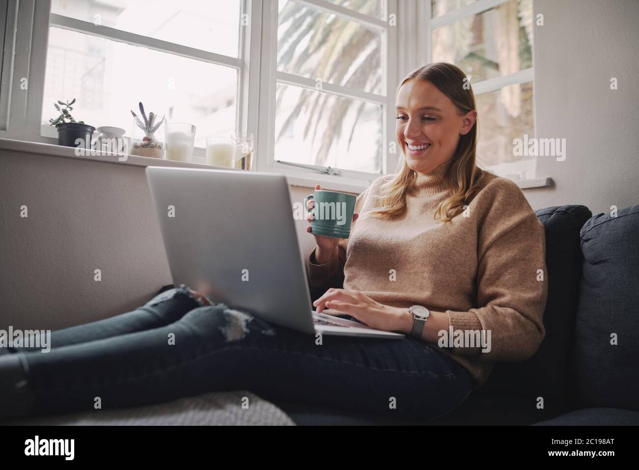 Donna d'affari autoisolata che lavora su computer portatile seduto a casa tenendo una tazza di caffè in mano durante la quarantena durante il covid-19 e il coronavirus Foto Stock