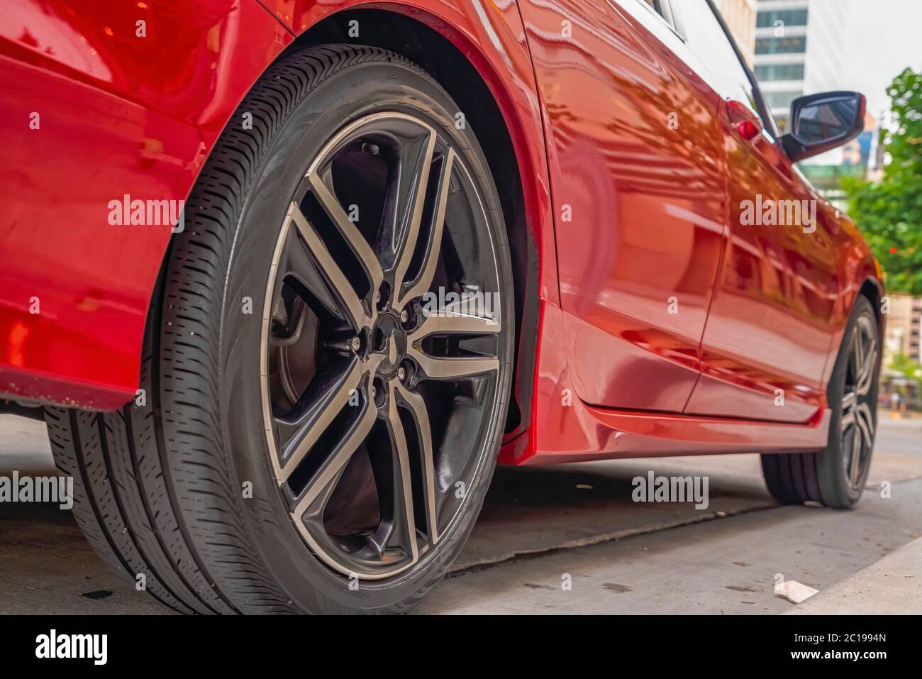 Esterno dell'auto rosso lucido con primo piano delle ruote in gomma nera contro la strada Foto Stock