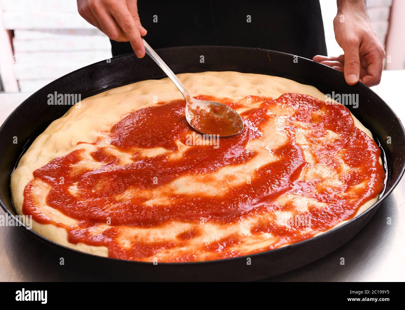 Chef stendendo il pomodoro su una base di pizza in una padella in un ristorante o pizzeria da vicino sulle sue mani Foto Stock