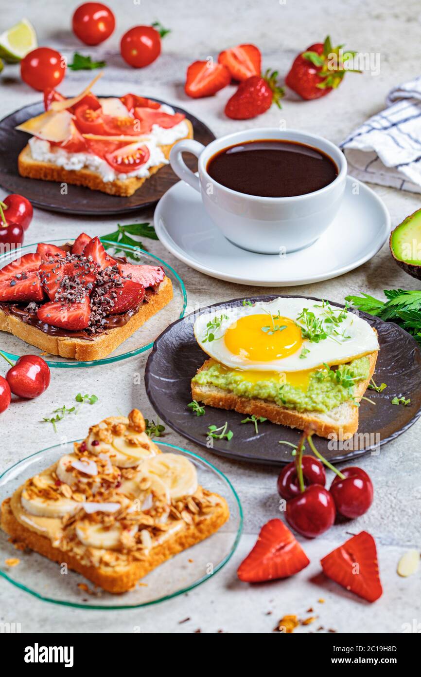 Colazione toast diversi con frutti di bosco, formaggio, uova e frutta, sfondo chiaro. Concetto di tavolo per la colazione. Foto Stock