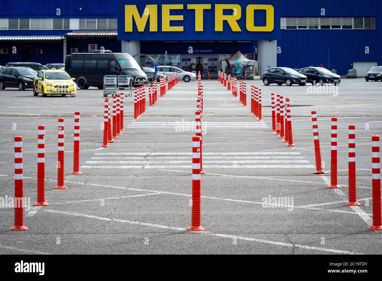 Zebra attraversando l'area pedonale e le racchette protettive arancioni al parcheggio che conducono all'entrata del Metro Cash e al negozio di articoli da trasporto a Sofia Foto Stock