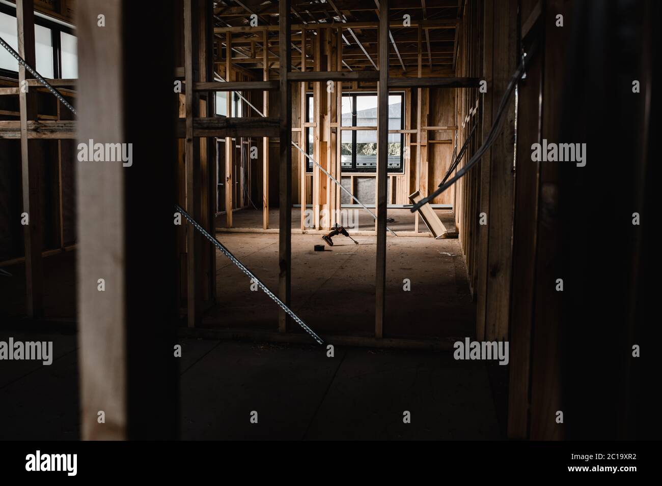 Un insieme di costruzione di una casa in costruzione con fili esposti e travi di legno, luce che splende sugli utensili Foto Stock