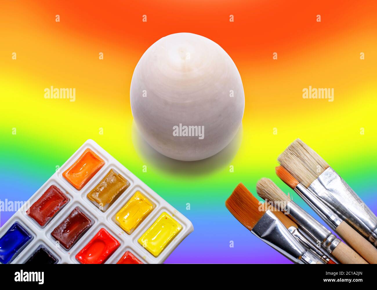 Non in legno dipinto di uovo sullo sfondo di un arcobaleno e un pennello con vernici, il concetto di colorare il mondo con vernici Foto Stock